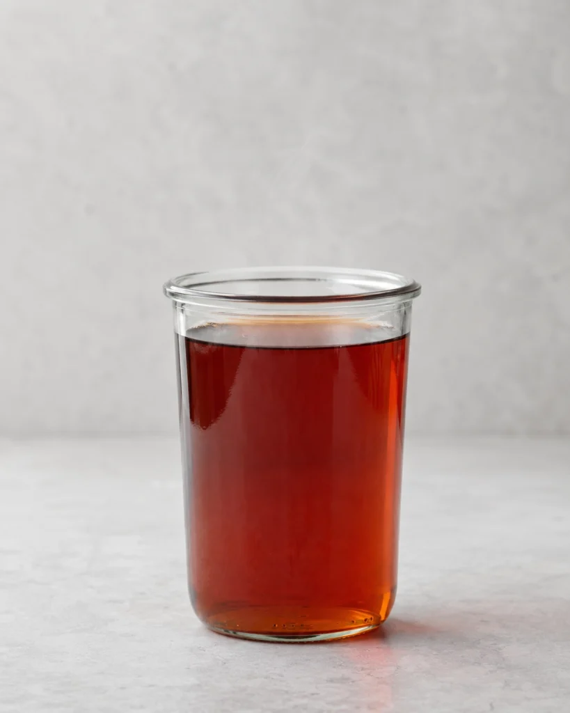 Vaso cilíndrico de vidrio lleno de té negro oscuro sobre una superficie de piedra gris clara.