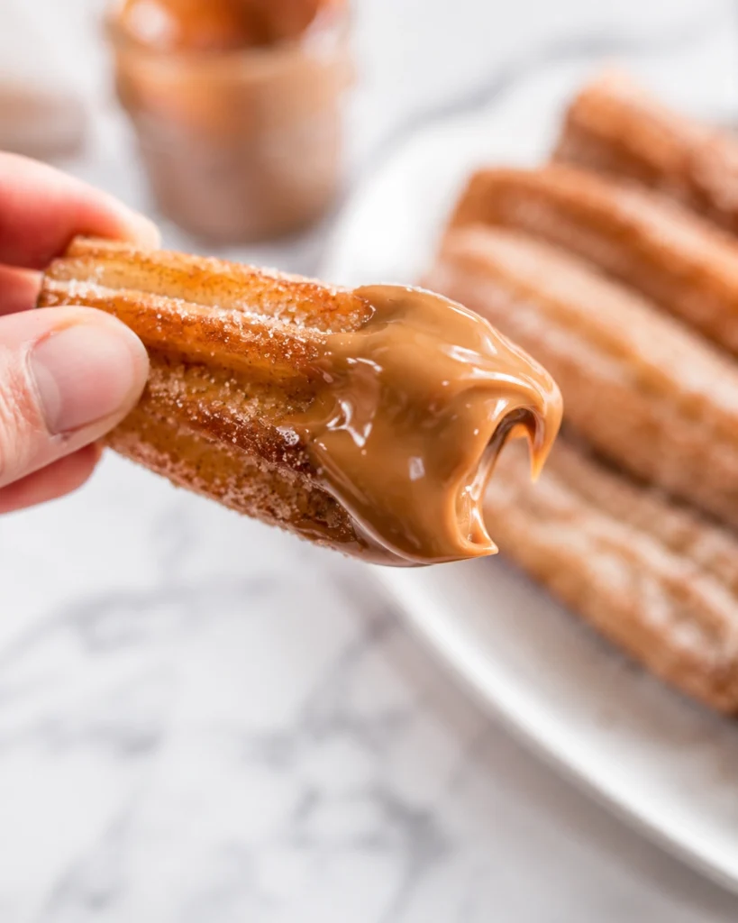 Churros caseros 5 Churros caseros dorados cubiertos con azúcar entrando en una taza de chocolate espeso.