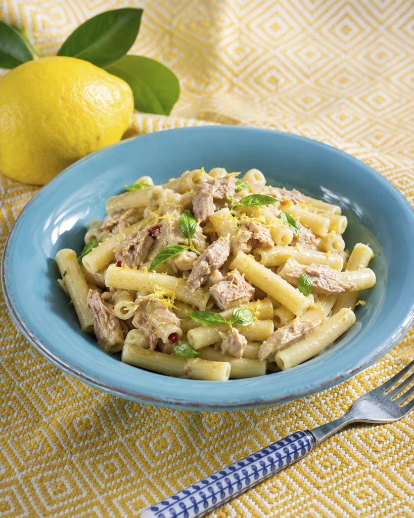 Pasta con atún y limón 2 Pasta con atún y limón servida en plato azul con ralladura cítrica, hojas de albahaca y un limón fresco al fondo.