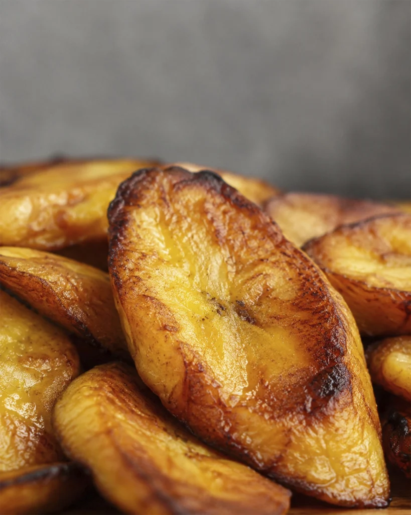 Plátanos maduros fritos 2 Plátanos maduros fritos en primer plano, con una tajada gruesa, dorada y caramelizada.