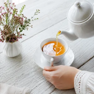 Tetera blanca sirviendo té caliente como base para preparar Té frío casero con frutas.