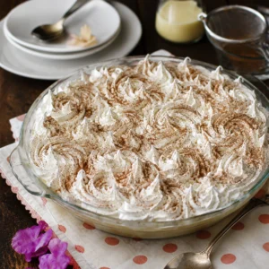 Torta tres leches con merengue blanco y canela en un molde de vidrio sobre mesa de madera.
